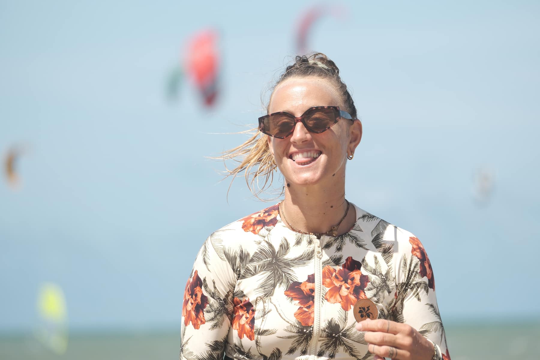 Woman smiling on the beach with kites in the sky behind her